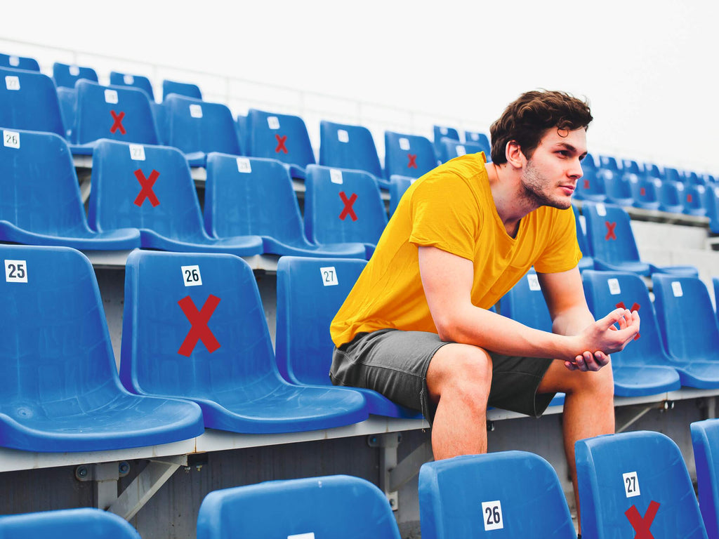 Red Durable Cross X stickers on blue stadium seats around a seated man
