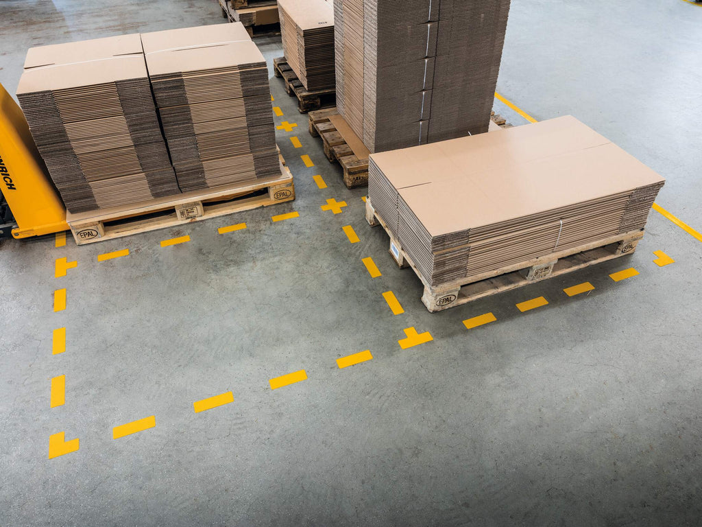 Yellow T, L, cross and stripe floor markings outlining pallet bays on a warehouse floor