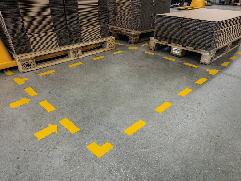 Yellow Durable arrows, stripes and L shapes marking a bay between pallets on a warehouse floor