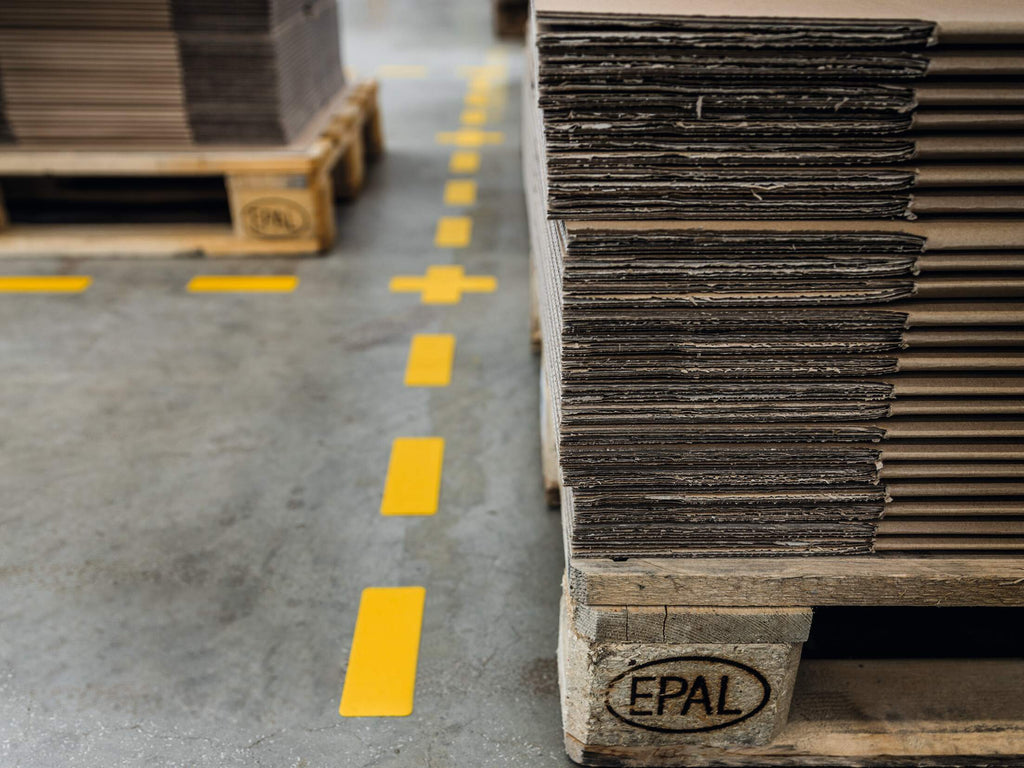 Durable yellow cross joining a dashed line of yellow stripes beside stacked pallets