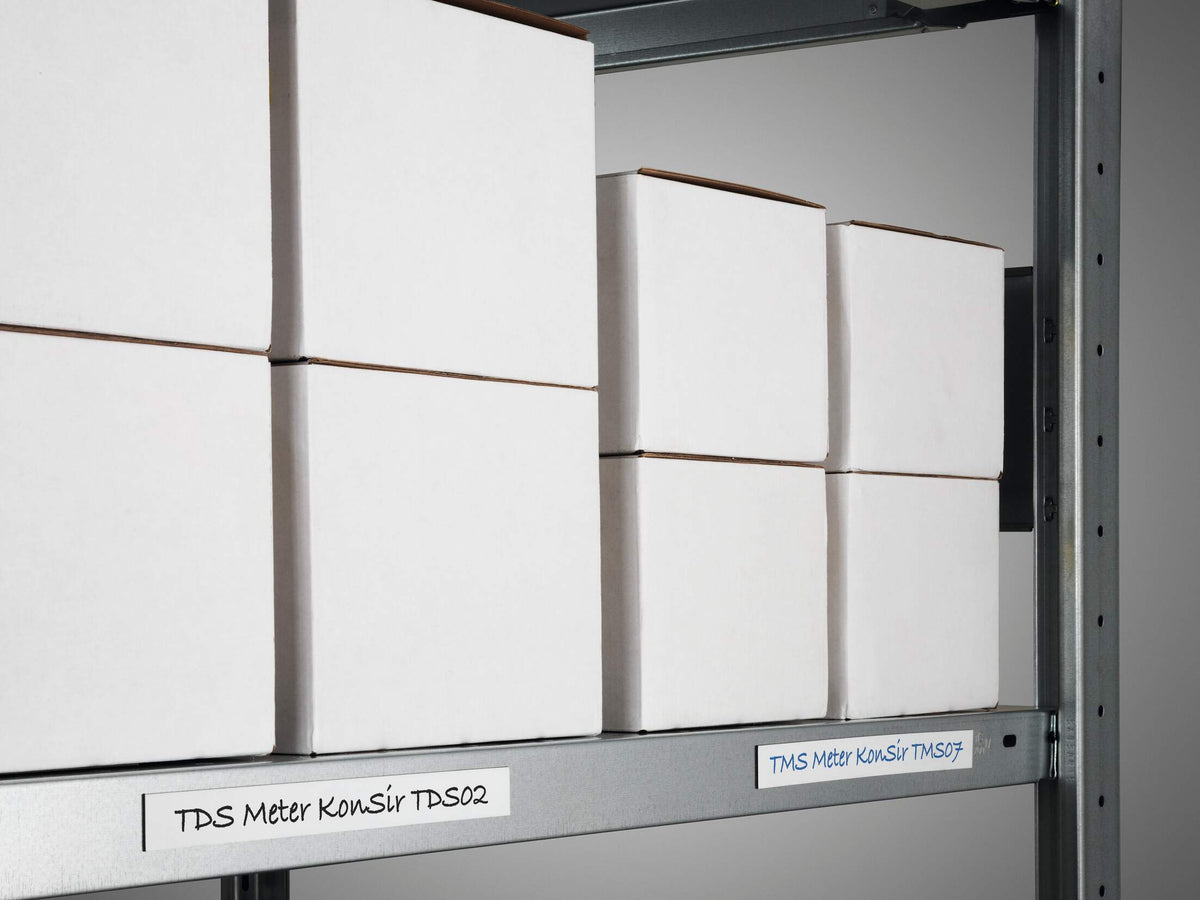 Handwritten labels cut from white magnetic tape on the edge of a steel shelf under boxes