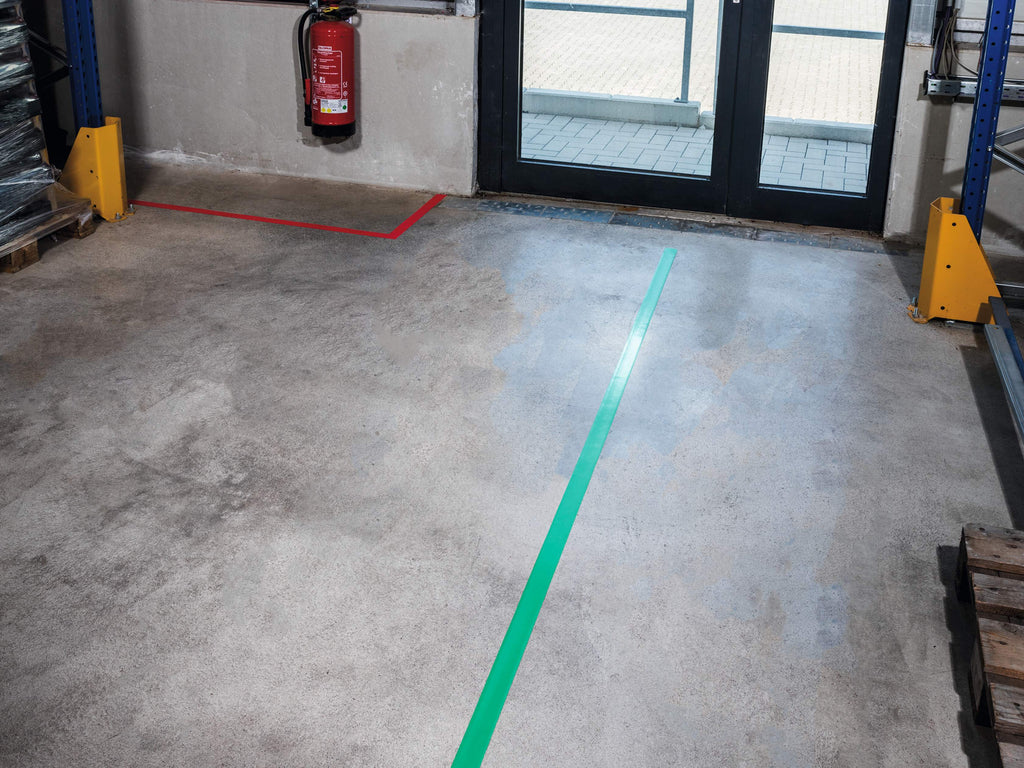 Green and red DURALINE STRONG lines on a concrete warehouse floor near racking and a glazed door