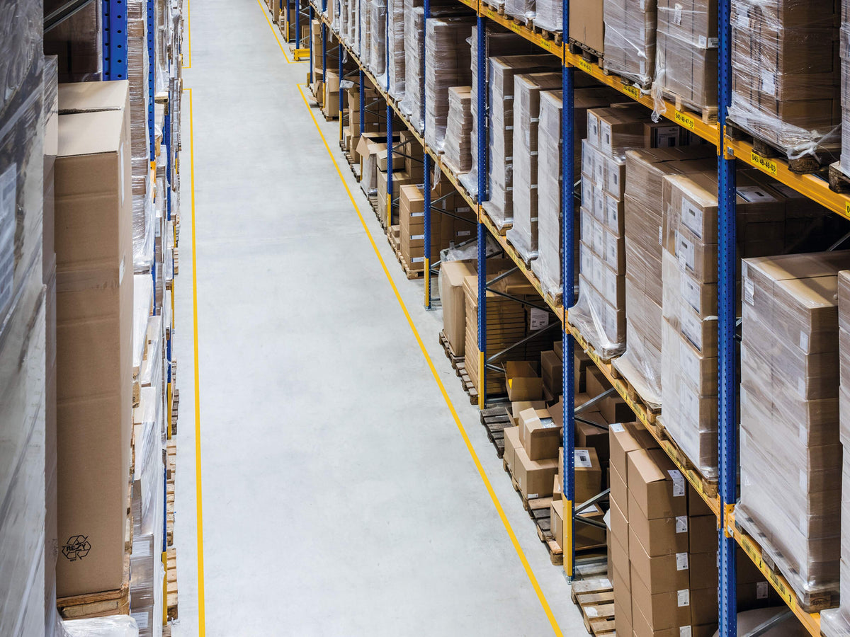 Yellow DURALINE STRONG lines along both sides of a warehouse aisle between loaded racking