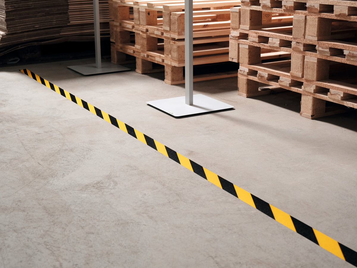 Yellow and black DURALINE 50/07 tape along a concrete floor beside stacked timber pallets