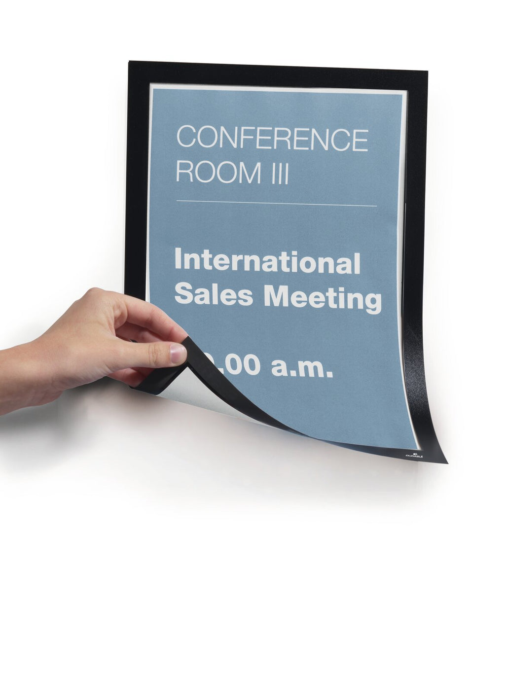 Hand lifting the corner of a black Durable Duraframe Magnetic A4 frame holding a Conference Room III International Sales Meeting notice