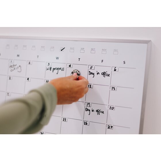 Close view of a Quartet monthly calendar planner with Day in office written in black marker as a hand places a round magnet on the grid