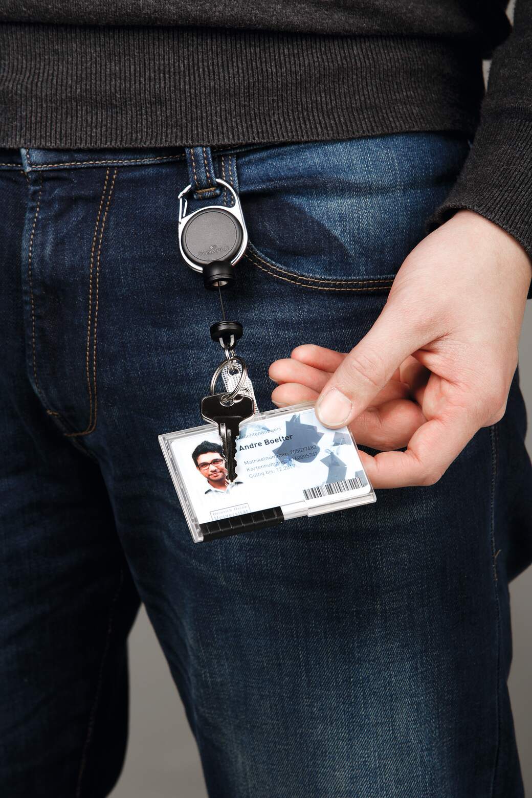 Durable Extra Strong badge reel clipped at the waist, with keys and a staff photo card on the cord held out in one hand