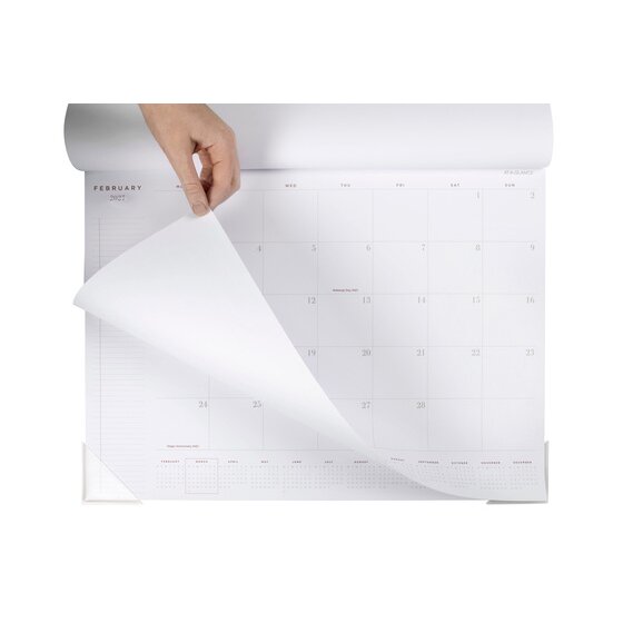 At-A-Glance AAG100127 desk pad with the February 2027 sheet being lifted back by hand, showing the notes column on the left and the clear corner protectors.
