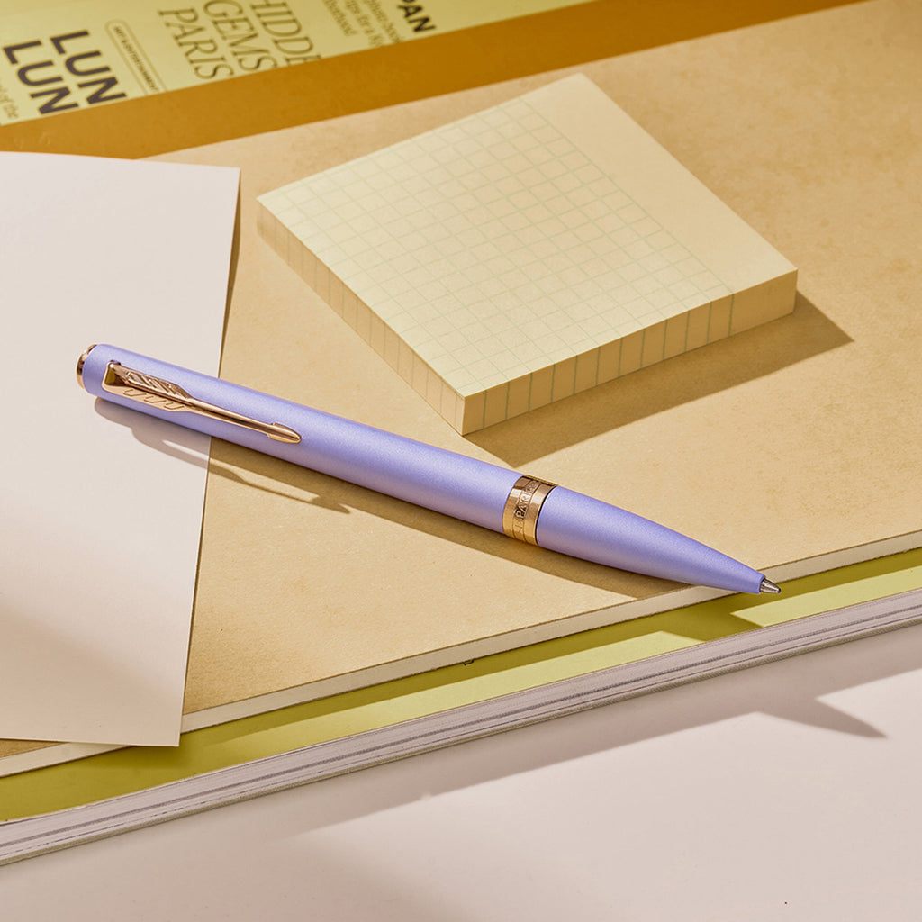 Lilac Meridian ballpoint in a styled desk setting, showing the pink gold clip and centre band