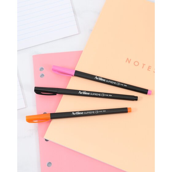 Three Artline Supreme Fine Pens with pink, black and orange ends lying on notebooks and a ruled pad